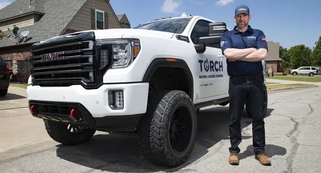Josh Hutchinson, owner of Torch Plumbing, Heating, & Cooling standing next to Torch company truck in a residential Owasso neighborhood.