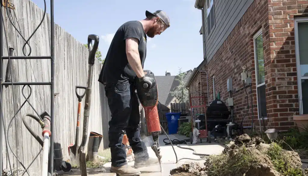 A Torch Plumbing, Heating, & Cooling Technician using jack hammer to remove concrete for a slab leak repair.
