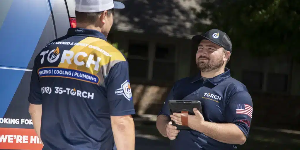 Two uniformed Torch Plumbing, Heating, & Cooling Technicians working together at a job site.